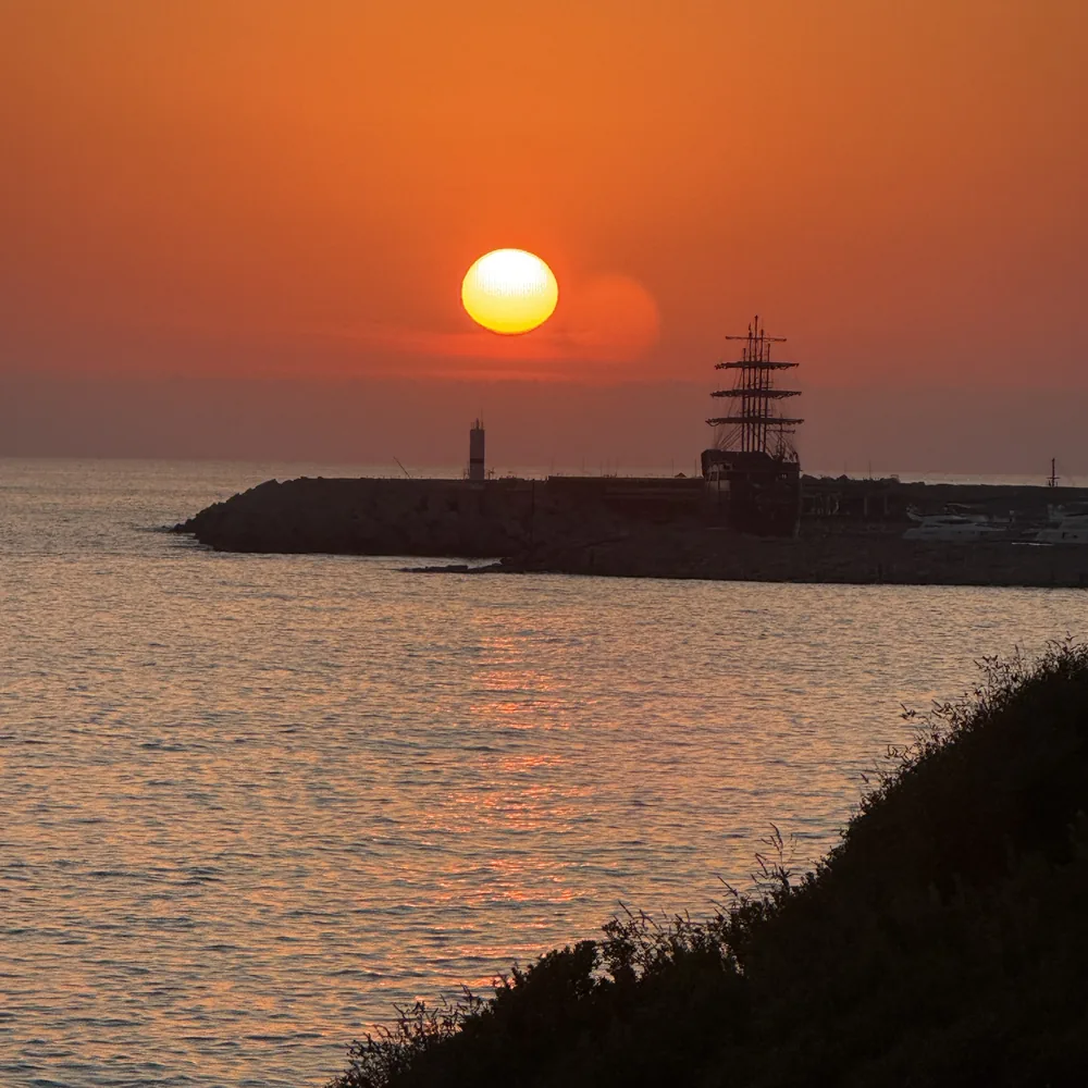 Zonsondergang boven het water met de silhouetten van een zeilschip en pier